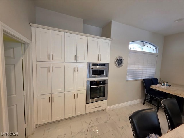 kitchen featuring white cabinetry, baseboards, and marble finish floor