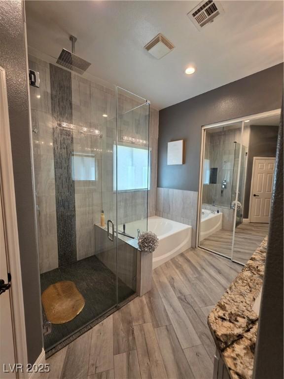 bathroom featuring a garden tub, wood finished floors, visible vents, and a stall shower