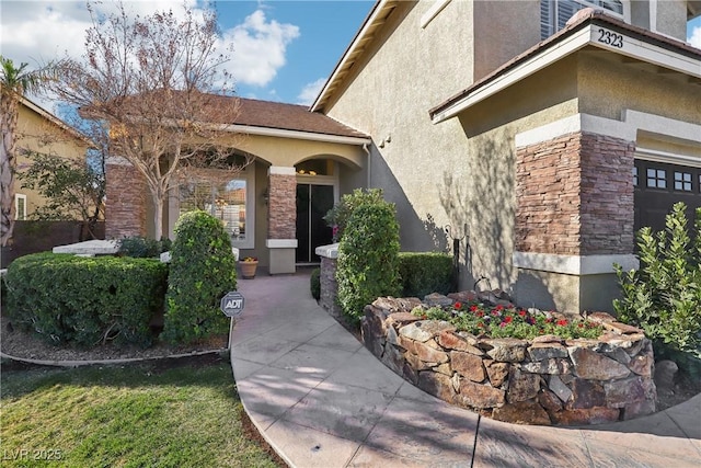 view of exterior entry with a garage, stone siding, and stucco siding