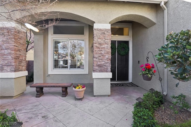 doorway to property with stone siding, stucco siding, and a patio