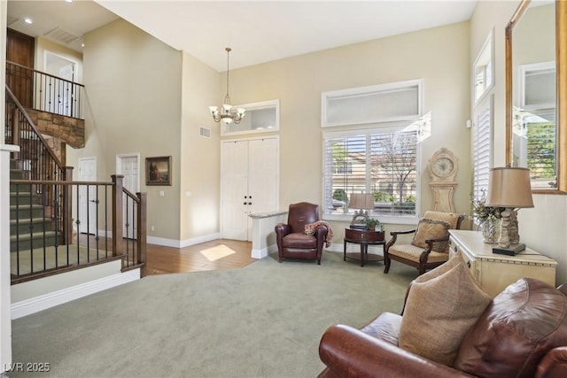 living area featuring a towering ceiling, visible vents, stairs, carpet, and an inviting chandelier