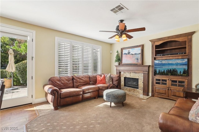 living area featuring ceiling fan, a fireplace, visible vents, and baseboards