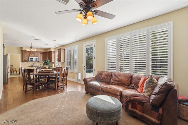 living room featuring ceiling fan with notable chandelier, light wood-type flooring, and baseboards