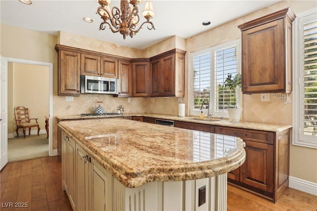 kitchen featuring light stone counters, a center island, stainless steel appliances, tasteful backsplash, and a sink