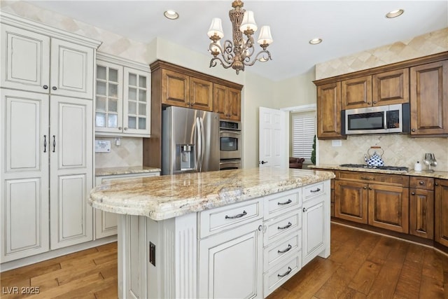 kitchen featuring light stone counters, stainless steel appliances, tasteful backsplash, glass insert cabinets, and hardwood / wood-style floors