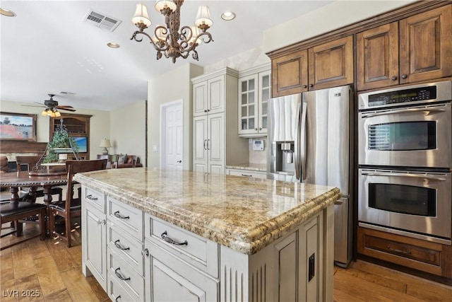 kitchen with visible vents, light wood-style flooring, appliances with stainless steel finishes, light stone counters, and a center island