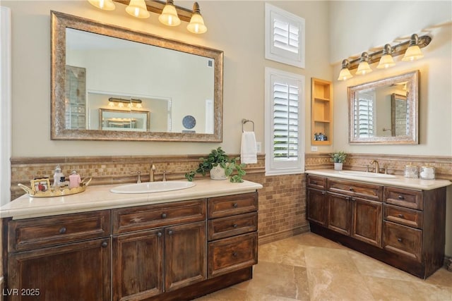 bathroom with a wainscoted wall, two vanities, a sink, and tile walls