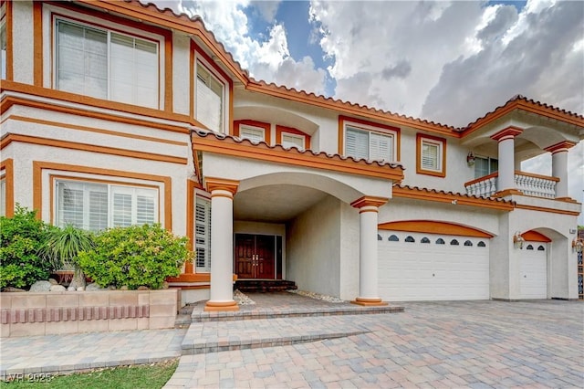 mediterranean / spanish home featuring a garage, decorative driveway, a tile roof, and stucco siding