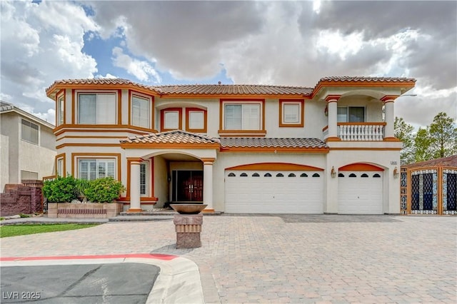 mediterranean / spanish-style house with an attached garage, a tile roof, decorative driveway, and stucco siding