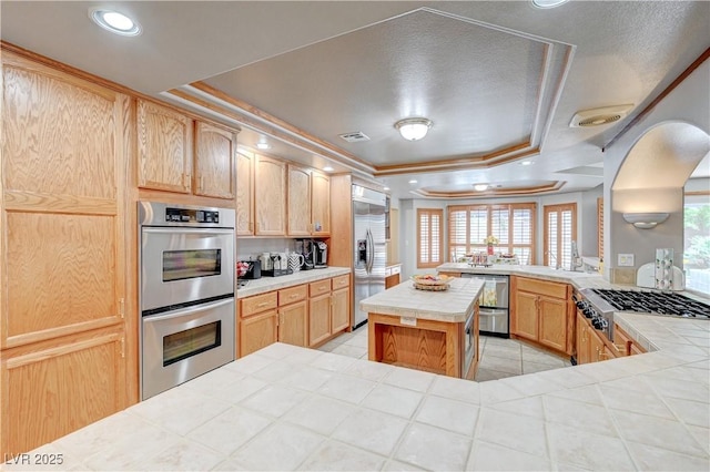 kitchen featuring stainless steel appliances, tile counters, a raised ceiling, and light brown cabinetry