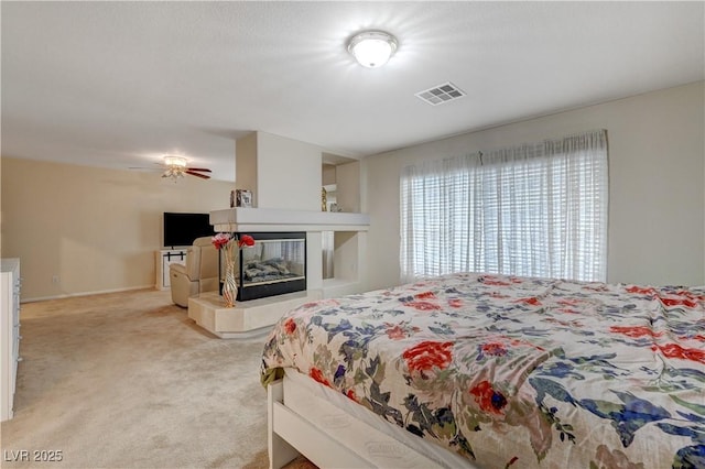 bedroom featuring visible vents, light carpet, and a tiled fireplace