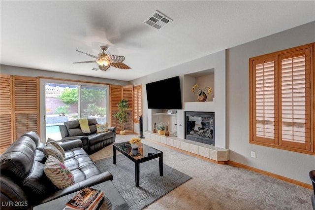 living area featuring visible vents, a tiled fireplace, a ceiling fan, carpet flooring, and baseboards