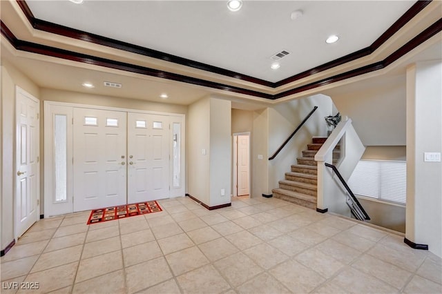 entrance foyer with a tray ceiling, crown molding, visible vents, stairway, and baseboards