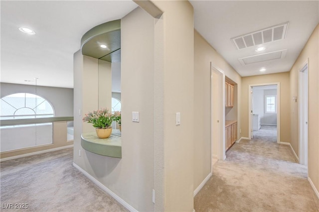 hall with light carpet, a wealth of natural light, visible vents, and baseboards