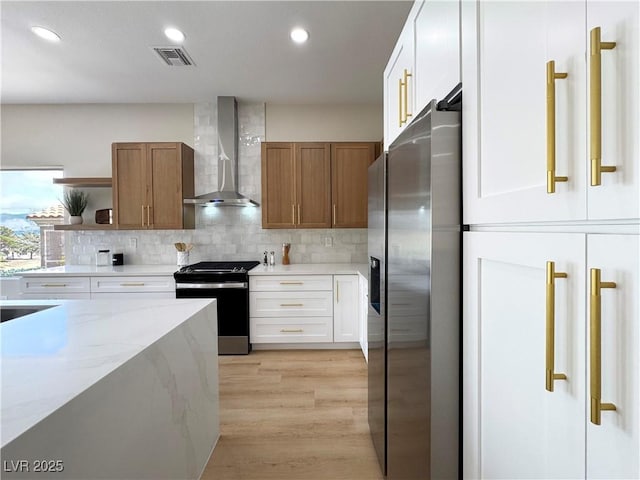 kitchen featuring visible vents, decorative backsplash, stainless steel refrigerator with ice dispenser, gas range, and wall chimney range hood