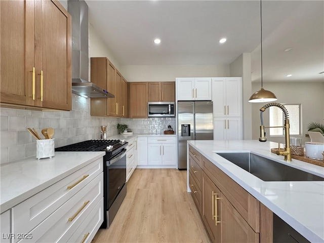 kitchen featuring tasteful backsplash, wall chimney range hood, light wood-style flooring, appliances with stainless steel finishes, and a sink