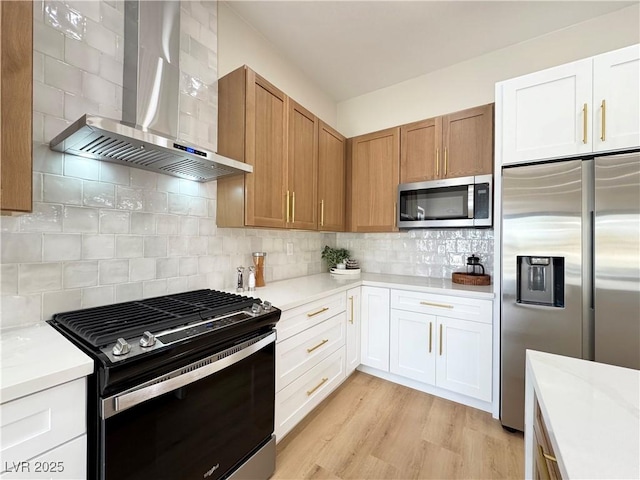 kitchen with light wood-type flooring, tasteful backsplash, appliances with stainless steel finishes, wall chimney exhaust hood, and light countertops