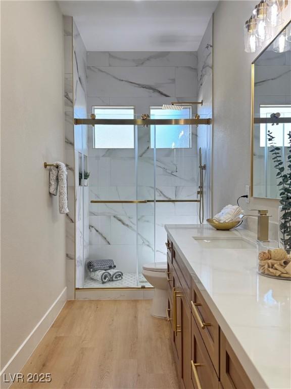 bathroom with vanity, wood finished floors, baseboards, a marble finish shower, and toilet