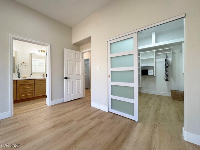 unfurnished bedroom with a closet, baseboards, light wood-style floors, and connected bathroom