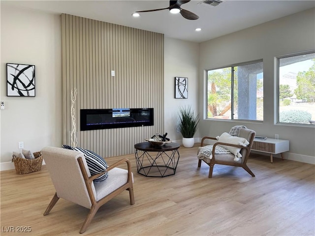 sitting room featuring visible vents, wood finished floors, a glass covered fireplace, recessed lighting, and baseboards