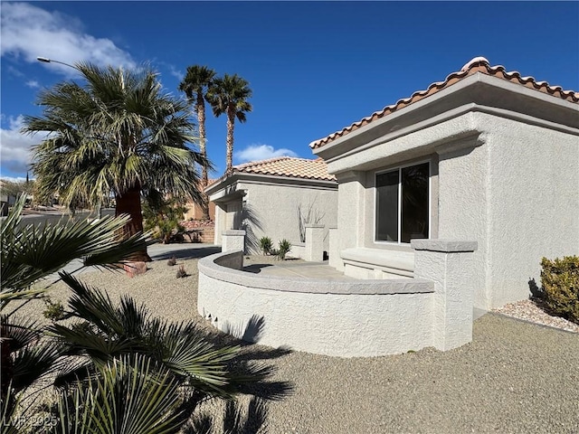 back of house with stucco siding and a tile roof