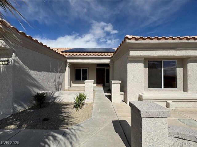 entrance to property featuring solar panels, a patio, and stucco siding