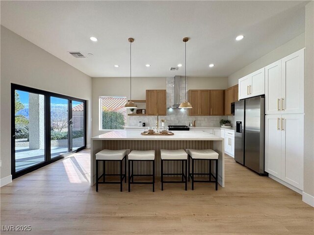 kitchen with visible vents, stainless steel fridge, wall chimney exhaust hood, light countertops, and decorative backsplash