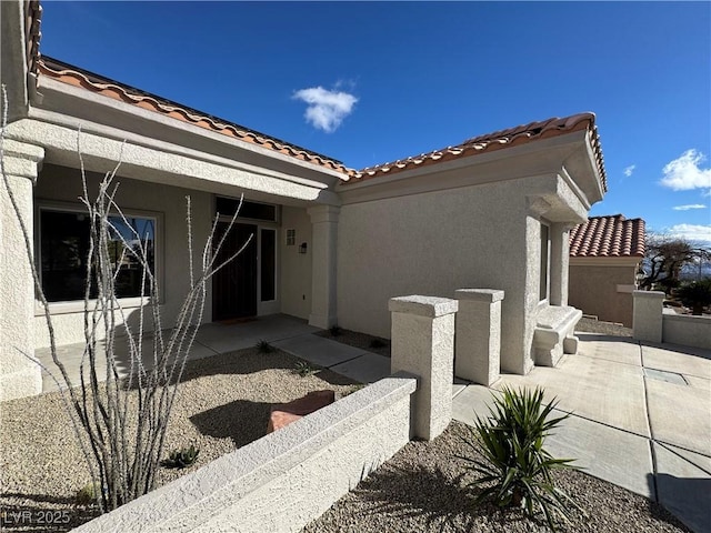 view of side of home featuring a patio area, stucco siding, and a tile roof