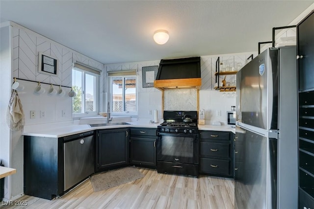 kitchen with light wood-style flooring, appliances with stainless steel finishes, custom exhaust hood, light countertops, and a sink