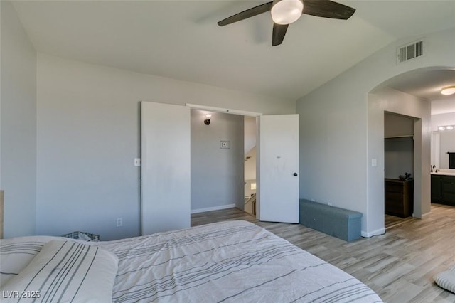 bedroom featuring visible vents, arched walkways, ensuite bathroom, vaulted ceiling, and light wood-style floors