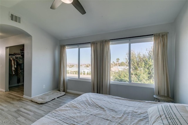 bedroom with arched walkways, a walk in closet, visible vents, wood finished floors, and baseboards