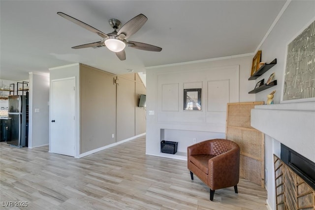 living area with light wood-style floors, ceiling fan, a fireplace, and ornamental molding