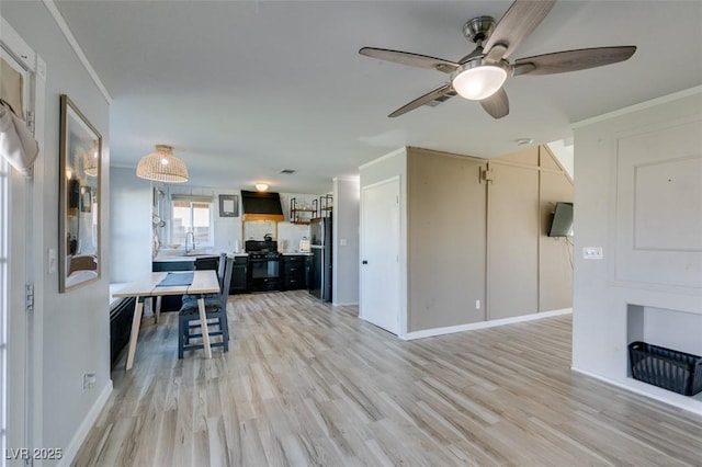 interior space with a sink, light wood-style floors, wall chimney exhaust hood, black appliances, and crown molding