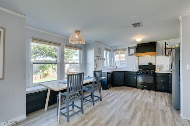 kitchen with black range with gas cooktop, visible vents, freestanding refrigerator, custom exhaust hood, and dark cabinetry