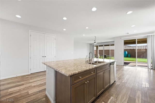 kitchen featuring recessed lighting, light wood-style flooring, stainless steel dishwasher, a sink, and light stone countertops