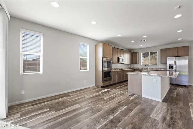 kitchen with dark wood-style floors, a kitchen island with sink, stainless steel appliances, and a sink