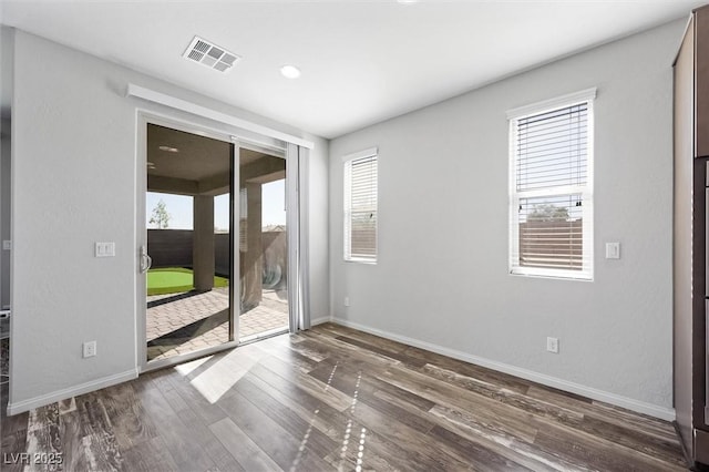 empty room featuring baseboards, wood finished floors, visible vents, and a healthy amount of sunlight