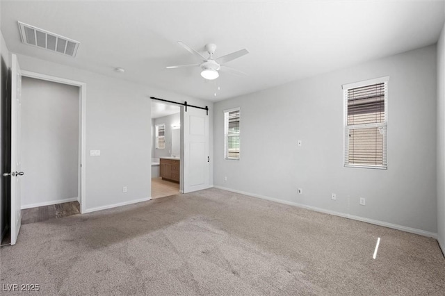 unfurnished bedroom with a barn door, visible vents, baseboards, ensuite bath, and carpet floors