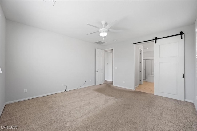 unfurnished bedroom featuring a barn door, light colored carpet, visible vents, baseboards, and ensuite bath