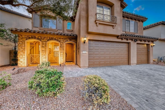 mediterranean / spanish home featuring a garage, a balcony, stone siding, decorative driveway, and stucco siding