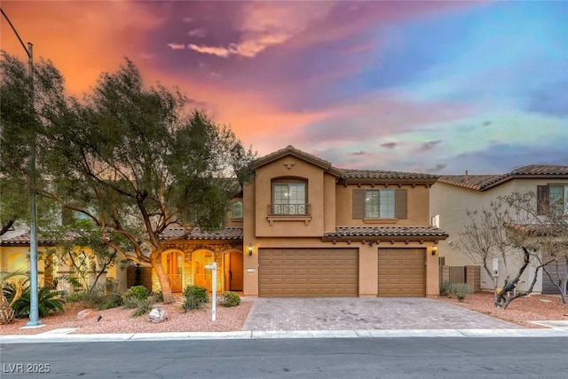 mediterranean / spanish house featuring a garage, decorative driveway, a tiled roof, and stucco siding