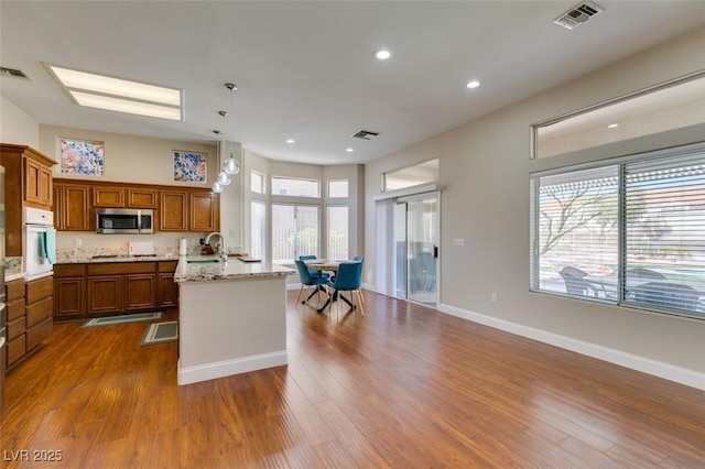 kitchen featuring oven, visible vents, brown cabinetry, stainless steel microwave, and dark wood finished floors