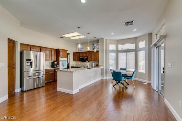 9816 Gerald Ct, Las Vegas, NV 89134 - kitchen with appliances with stainless steel finishes, brown cabinets, a peninsula, dark wood-type flooring, and hanging light fixtures