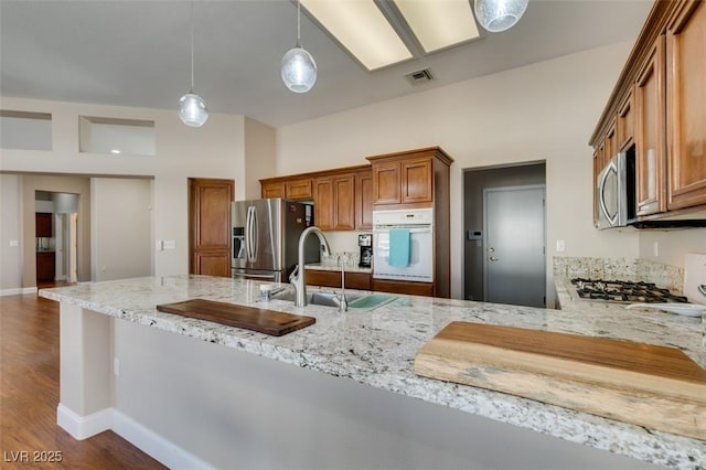 9816 Gerald Ct, Las Vegas, NV 89134 - kitchen featuring appliances with stainless steel finishes, brown cabinetry, light stone countertops, pendant lighting, and dark wood-style flooring