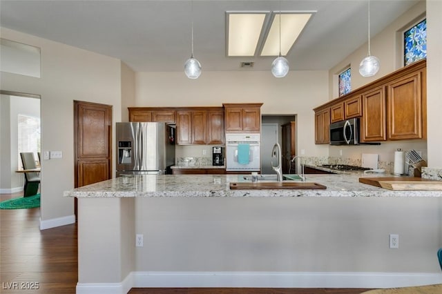 9816 Gerald Ct, Las Vegas, NV 89134 - kitchen with appliances with stainless steel finishes, a peninsula, brown cabinetry, light stone counters, and pendant lighting