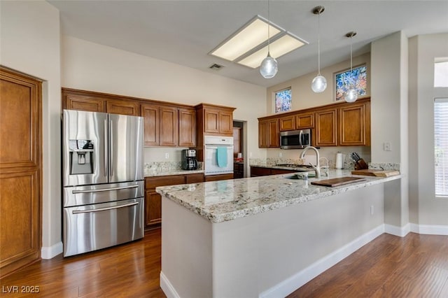 kitchen featuring brown cabinets, dark wood finished floors, stainless steel appliances, visible vents, and a peninsula