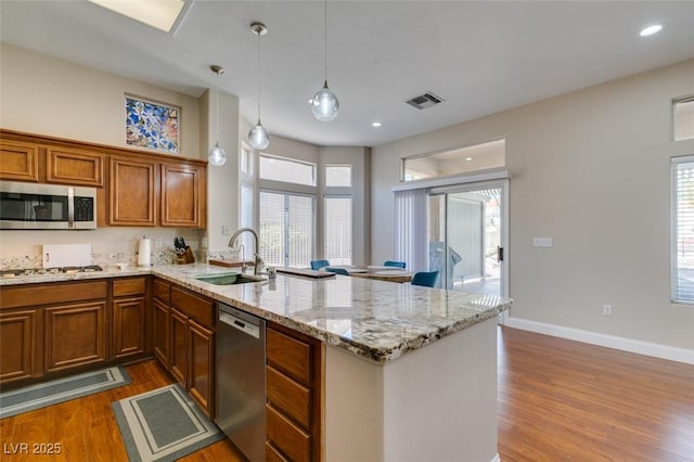 9816 Gerald Ct, Las Vegas, NV 89134 - kitchen with appliances with stainless steel finishes, a peninsula, dark wood-style flooring, brown cabinetry, and light stone counters