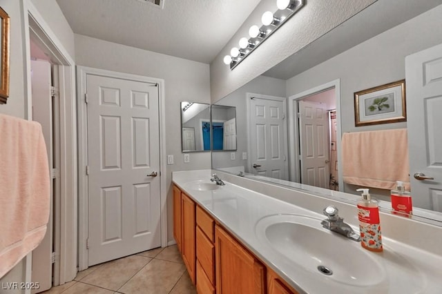 bathroom featuring double vanity, tile patterned flooring, a textured ceiling, and a sink