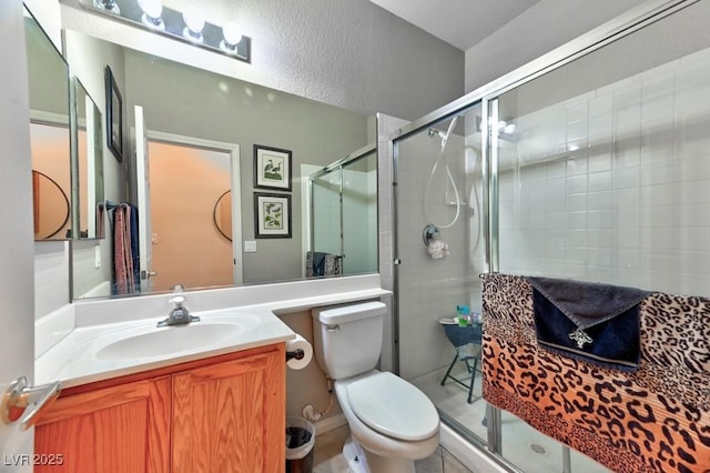 full bath featuring a stall shower, a textured wall, vanity, and toilet