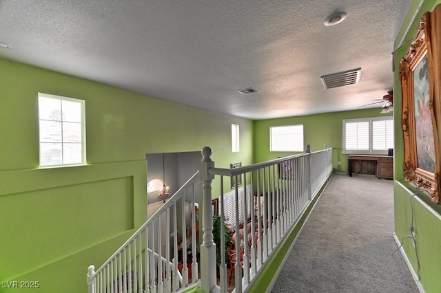 hallway with a textured ceiling, an upstairs landing, carpet flooring, and visible vents